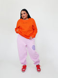 Person wearing an orange sweatshirt and blush sweatpants with a white background