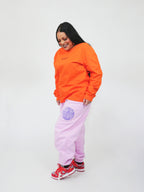 Person wearing an orange sweatshirt and blush sweatpants with a logo on a white background