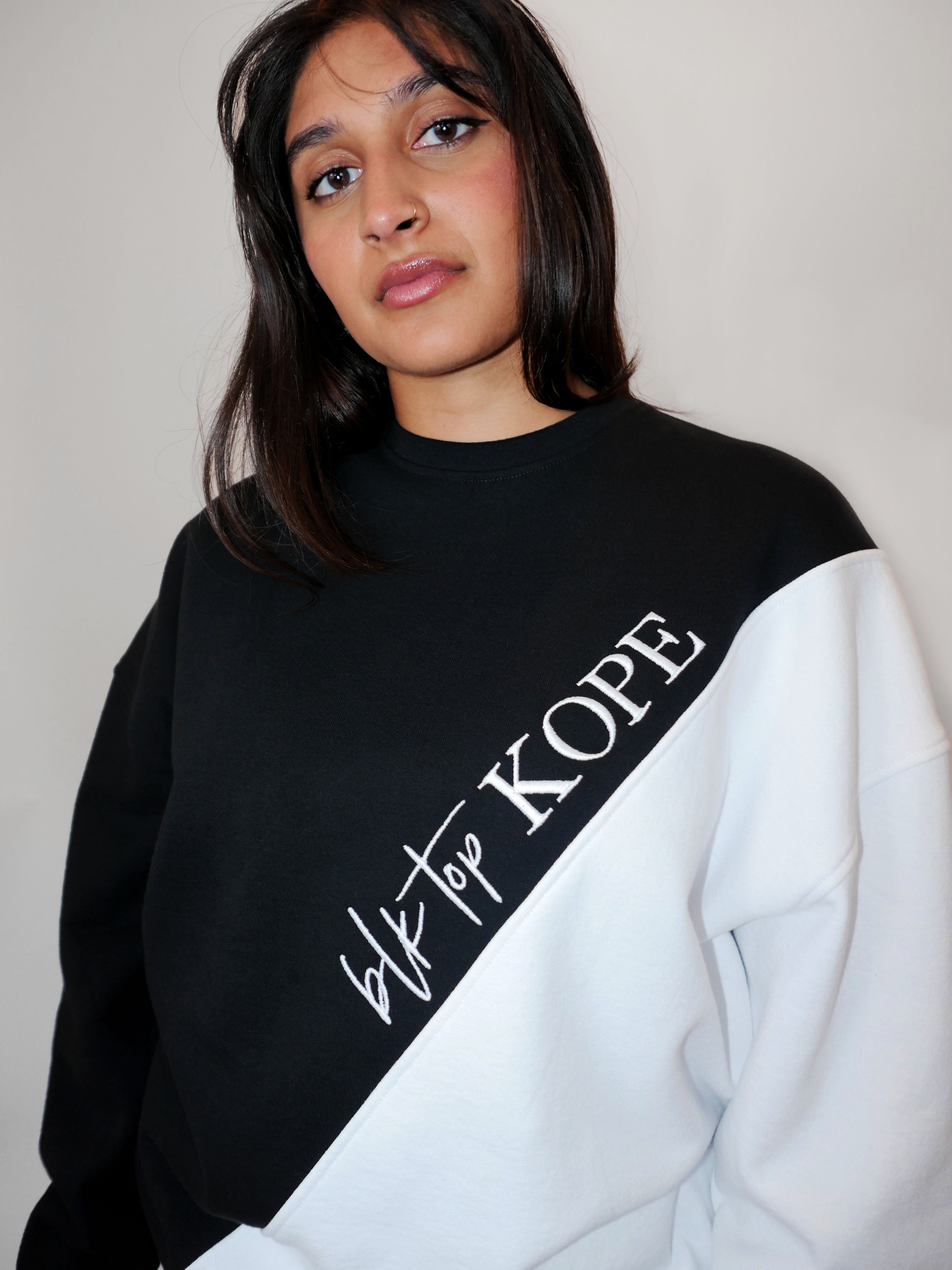 Woman wearing a black and white oversized crewneck with 'blk top KOPE' text.