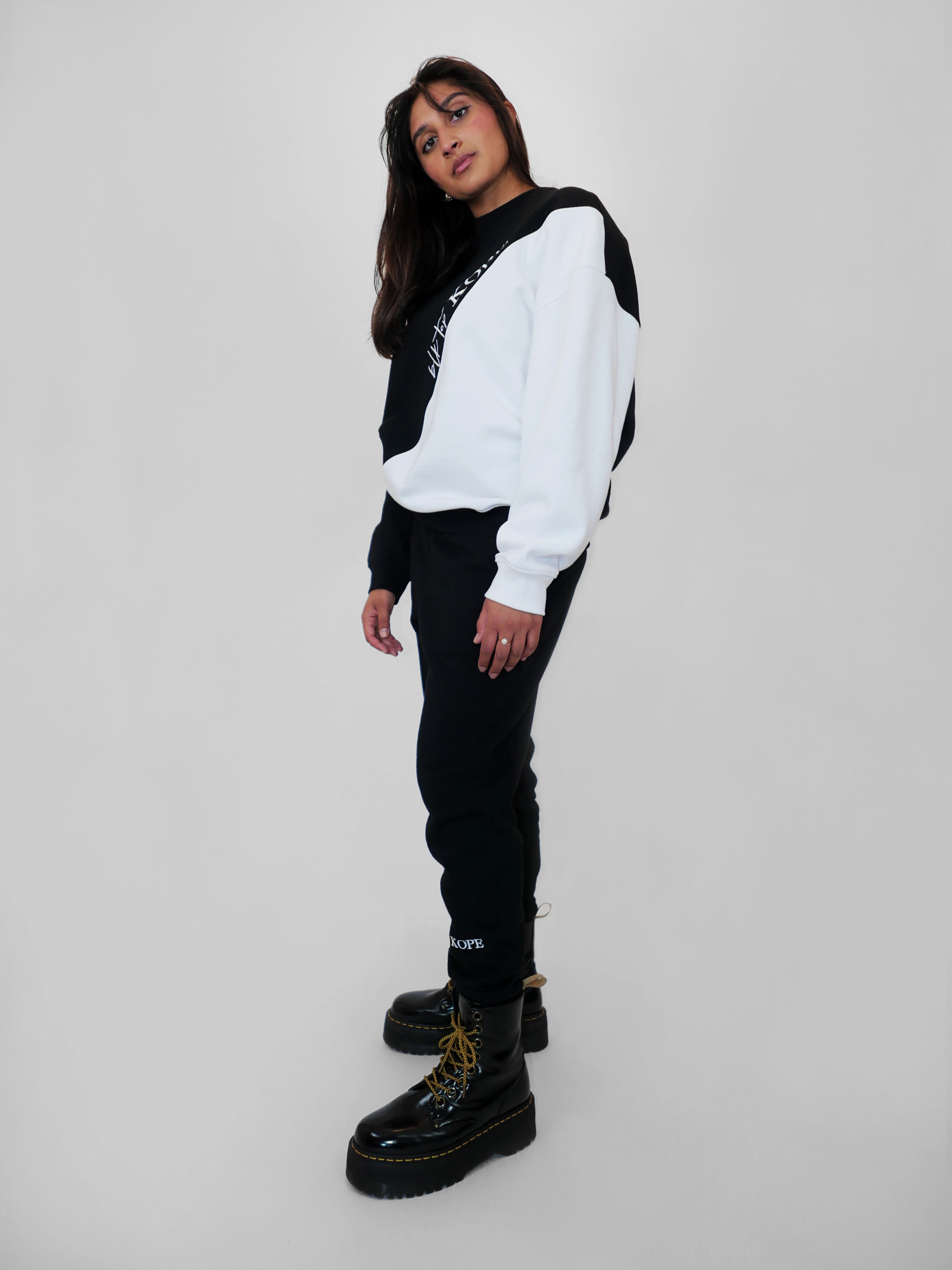 Woman wearing a black and white oversized crewneck and black sweatpants with black boots on a light gray background