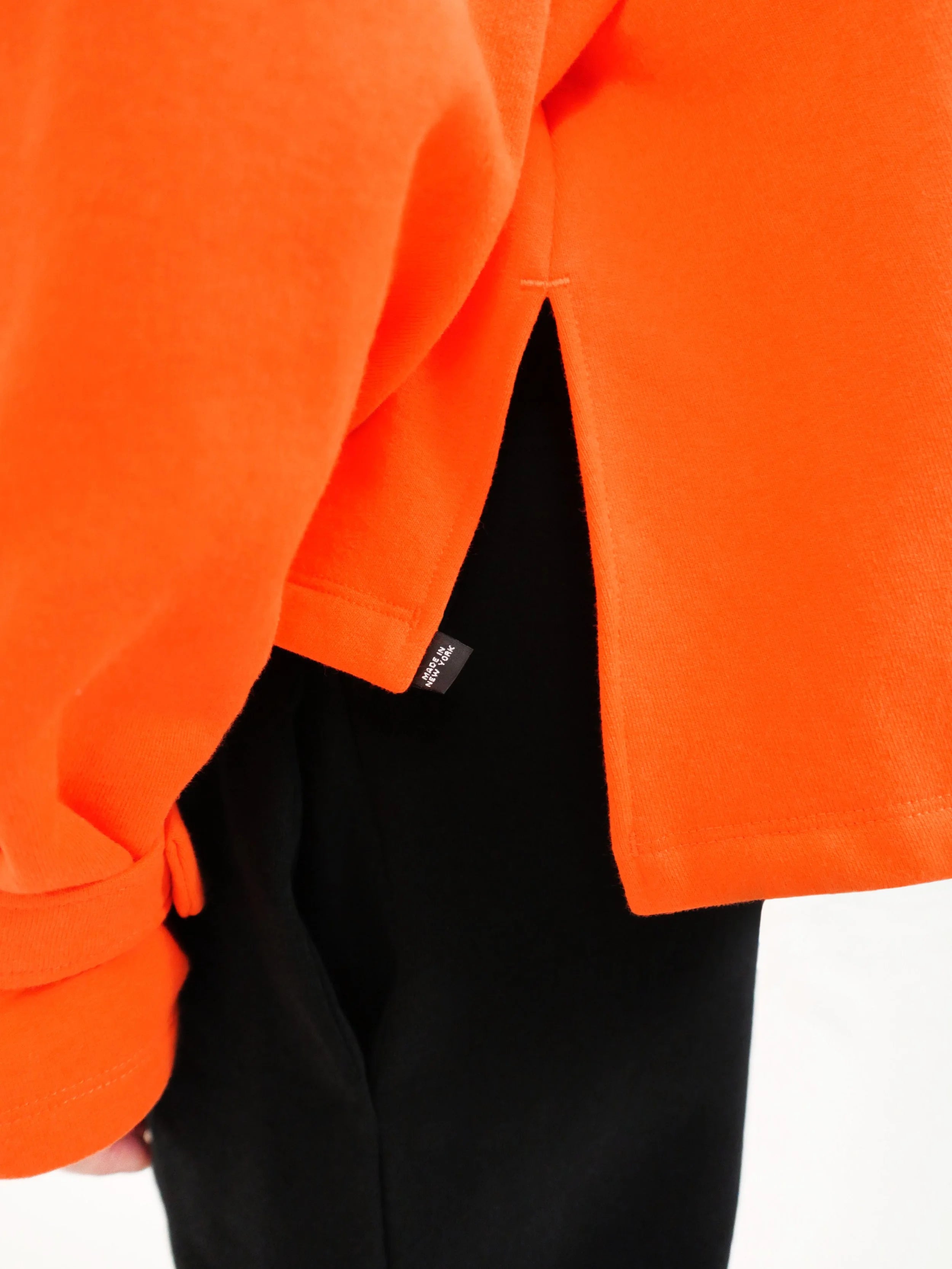 Close-up of an orange sweatshirt with a brand label on a white background