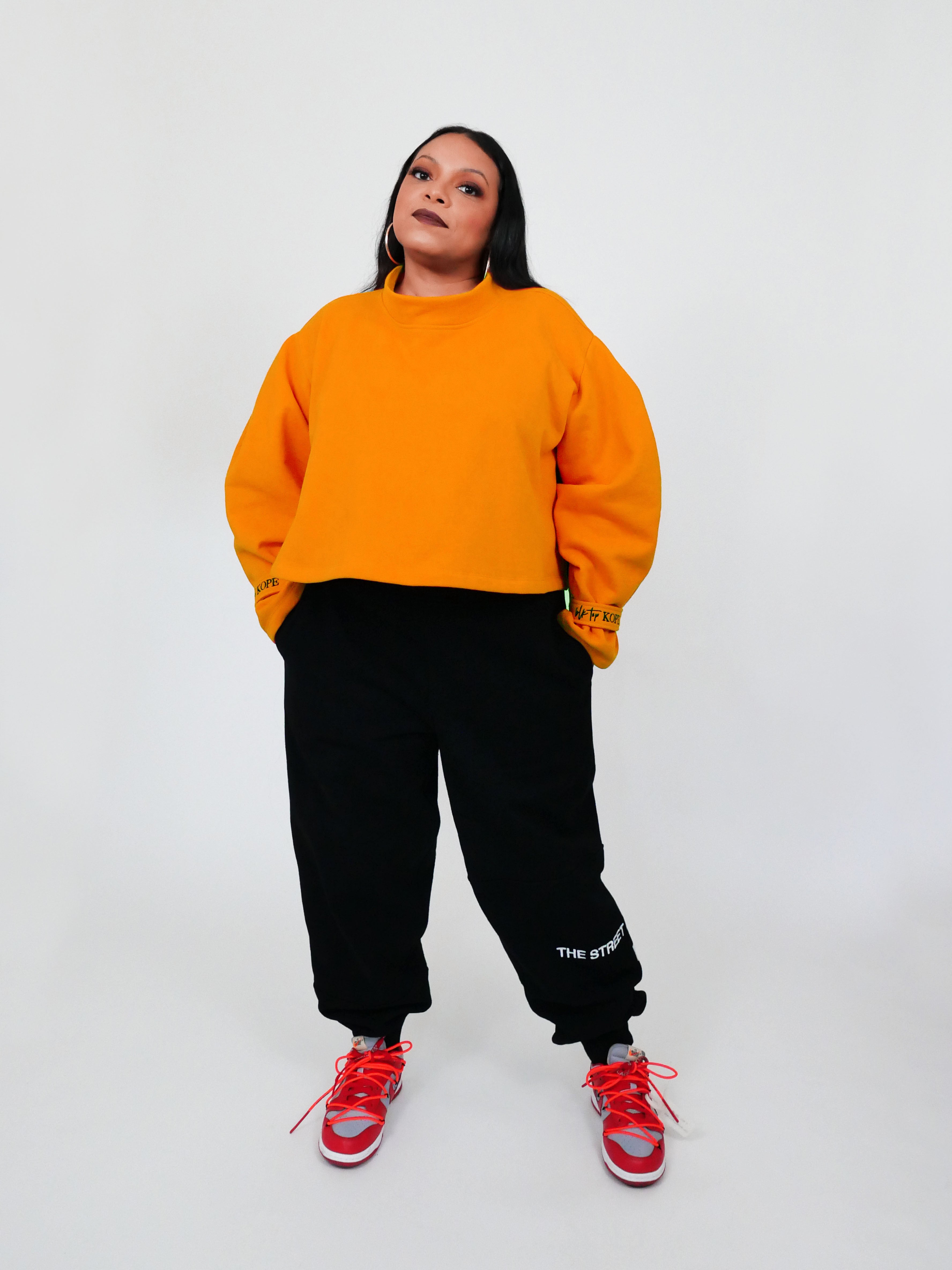 Person wearing a yellow sweatshirt, black sweatpants, and red sneakers on a white background