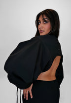 Person wearing a black oversized sweater with open back on a plain background