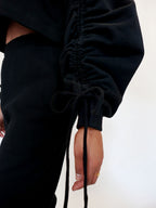 Person wearing a black outfit with tied sleeves against a white background