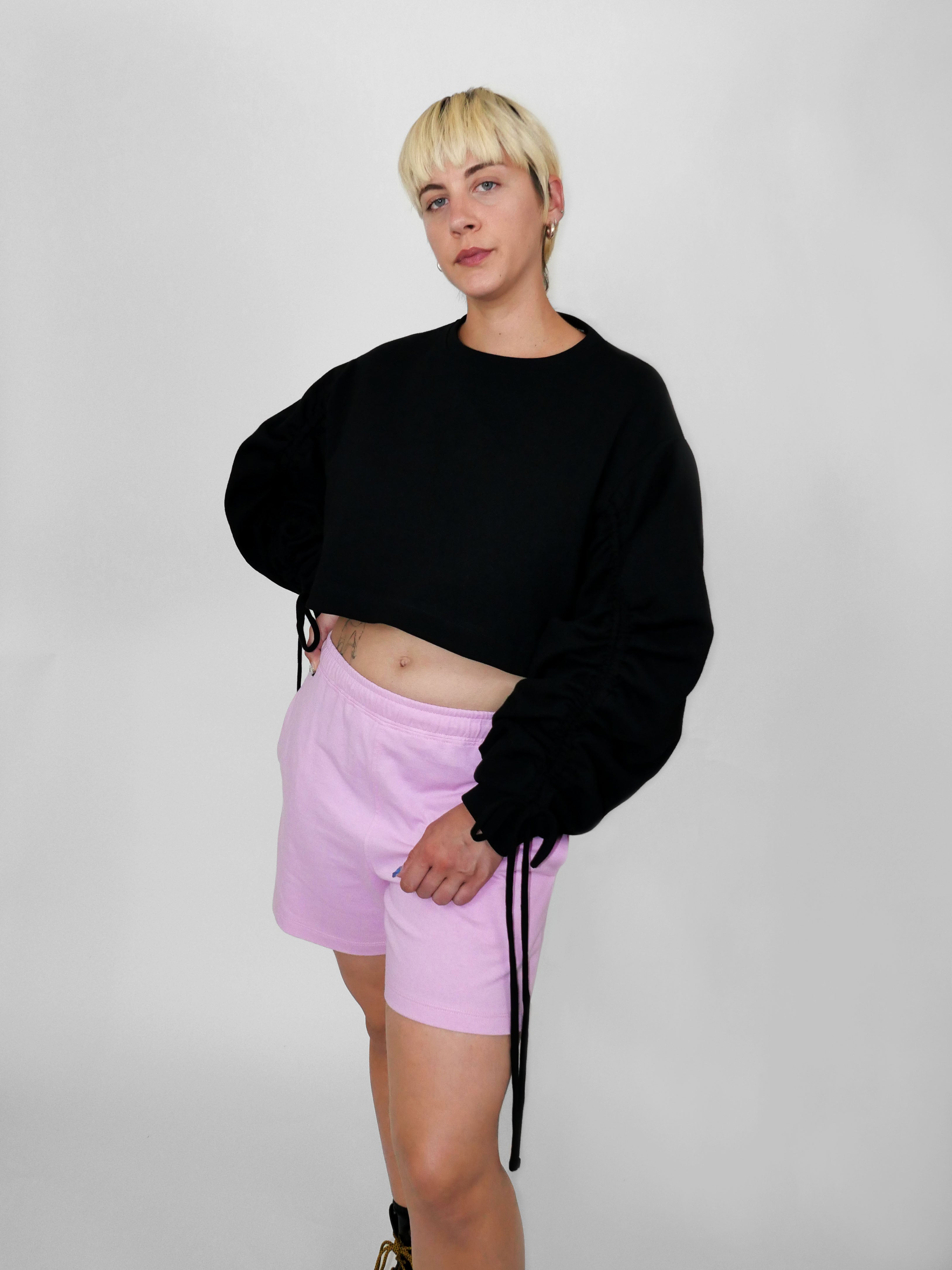 Person wearing a black sweater and pink shorts on a plain background