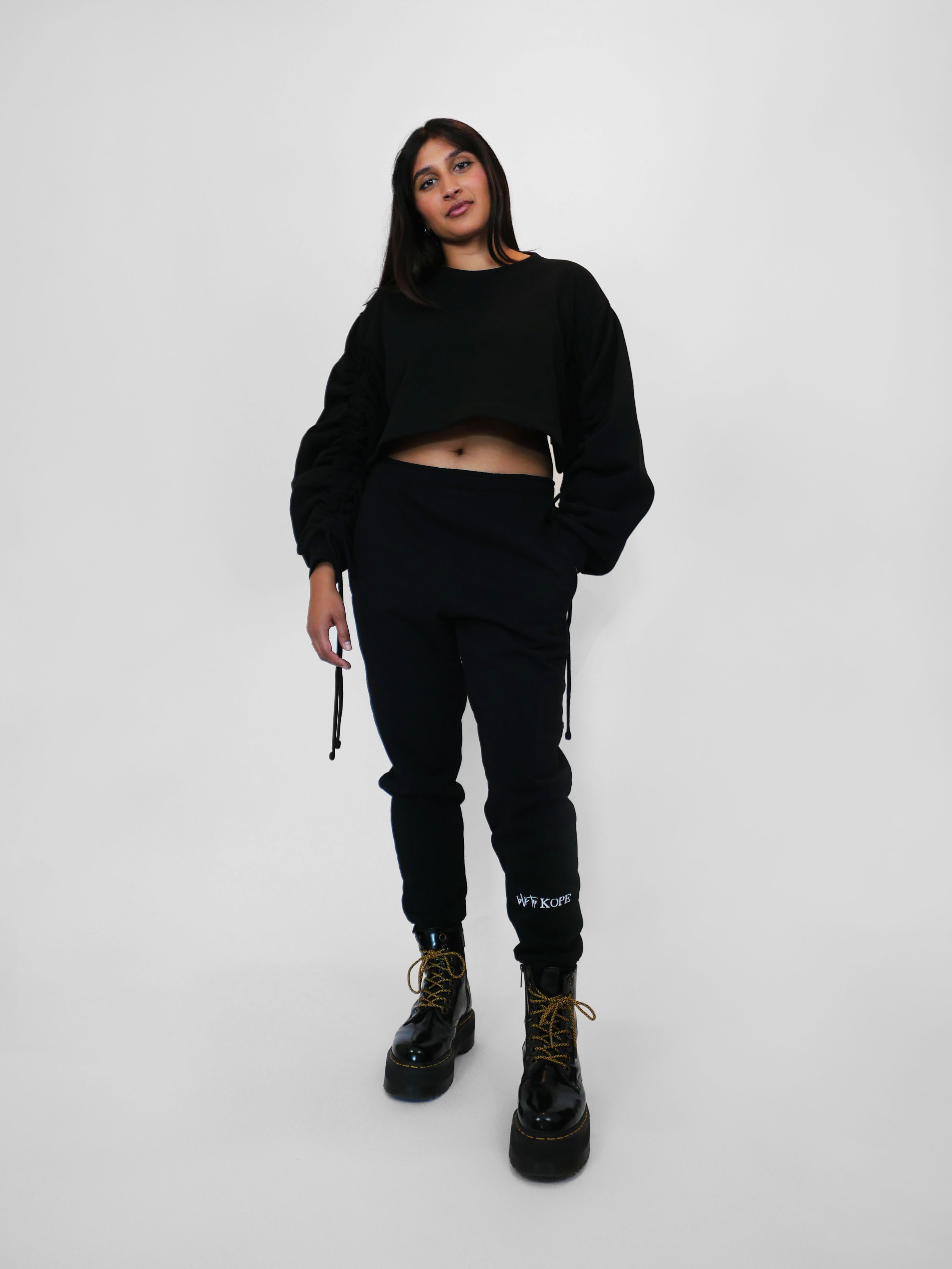 Person wearing a black outfit with text on sweatpants against a white background
