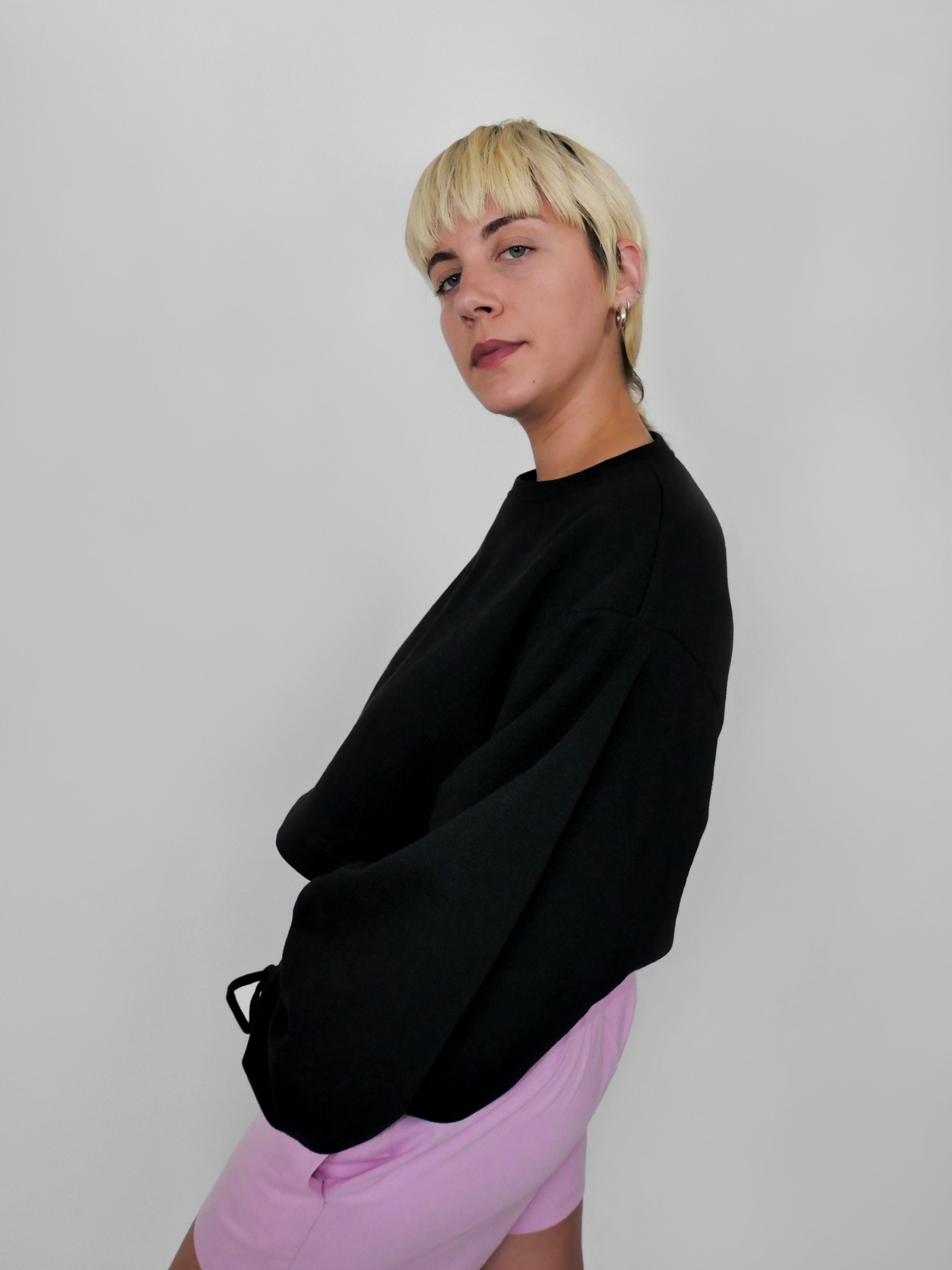 Person wearing a black sweater and pink pants against a plain background