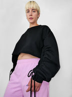 Person wearing a black cropped sweatshirt and pink pants against a plain background