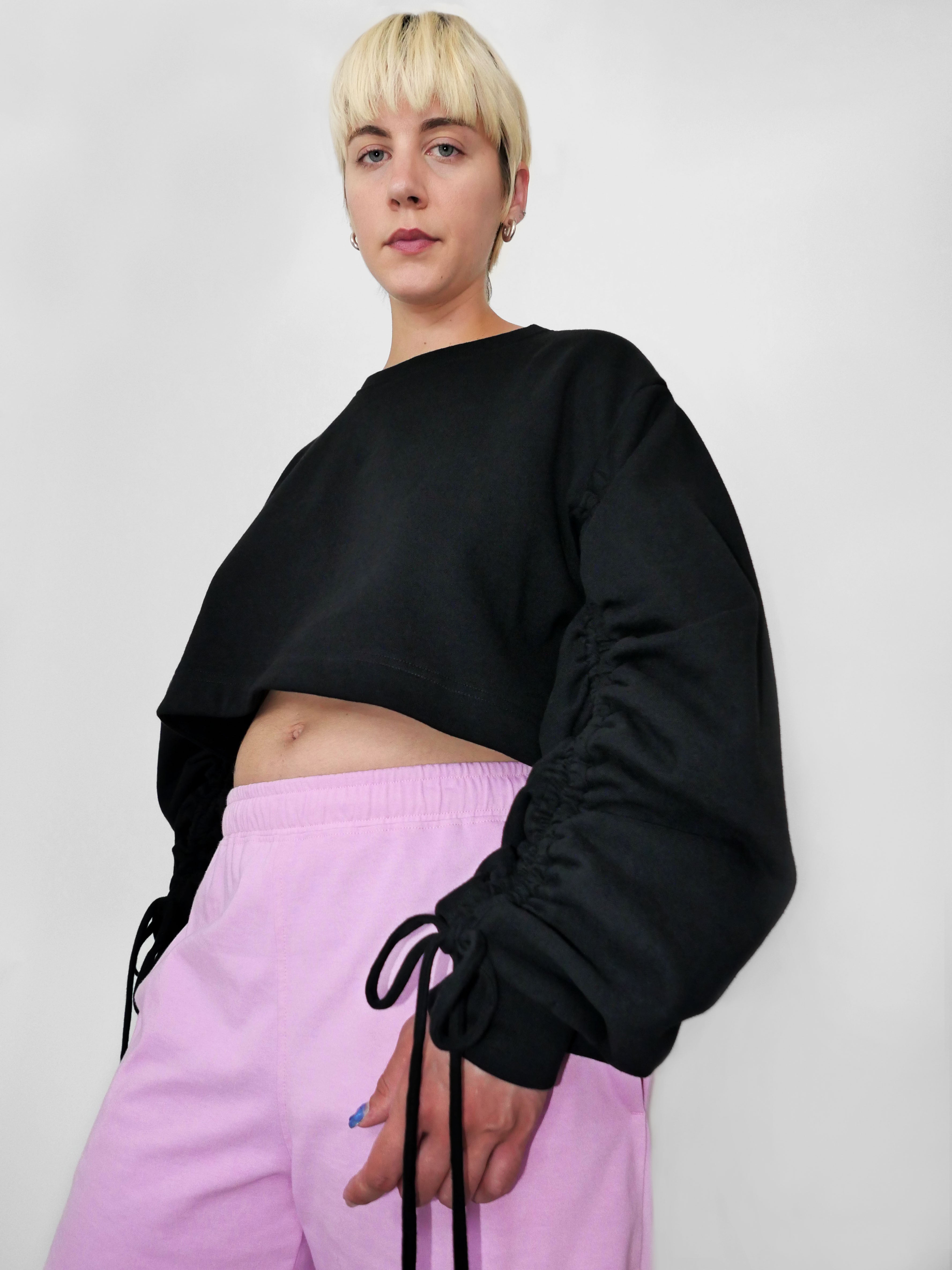 Person wearing a black cropped sweatshirt and pink pants against a plain background