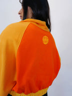 Person wearing an orange and yellow half zip-up with a logo on the back against a white background