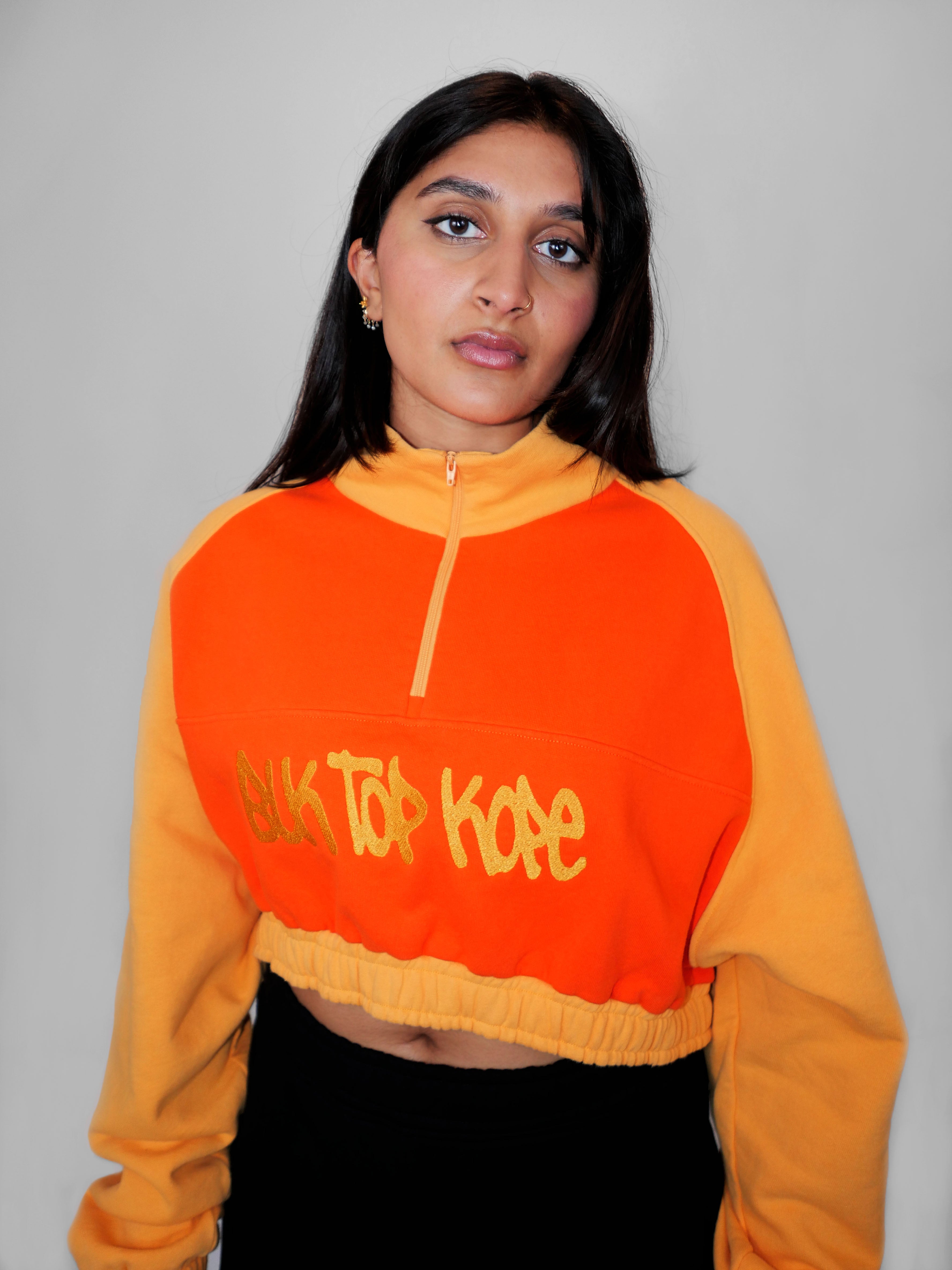 Person wearing a yellow and orange half zip-up with a logo design on a gray background