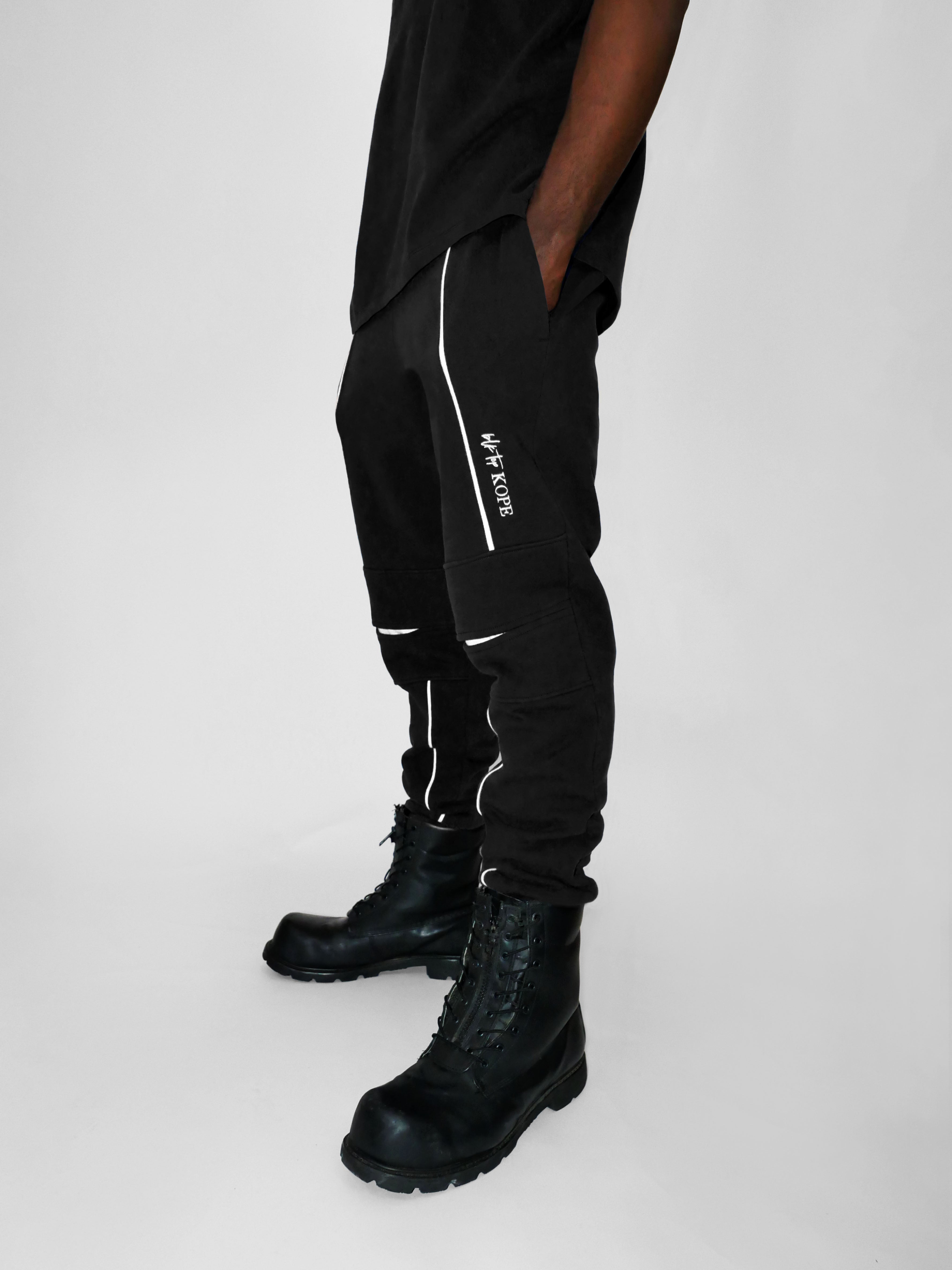 Person wearing black sweatpants with white text and black boots on a white background