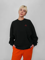 Person wearing a black sweatshirt with a red logo and orange pants against a plain background