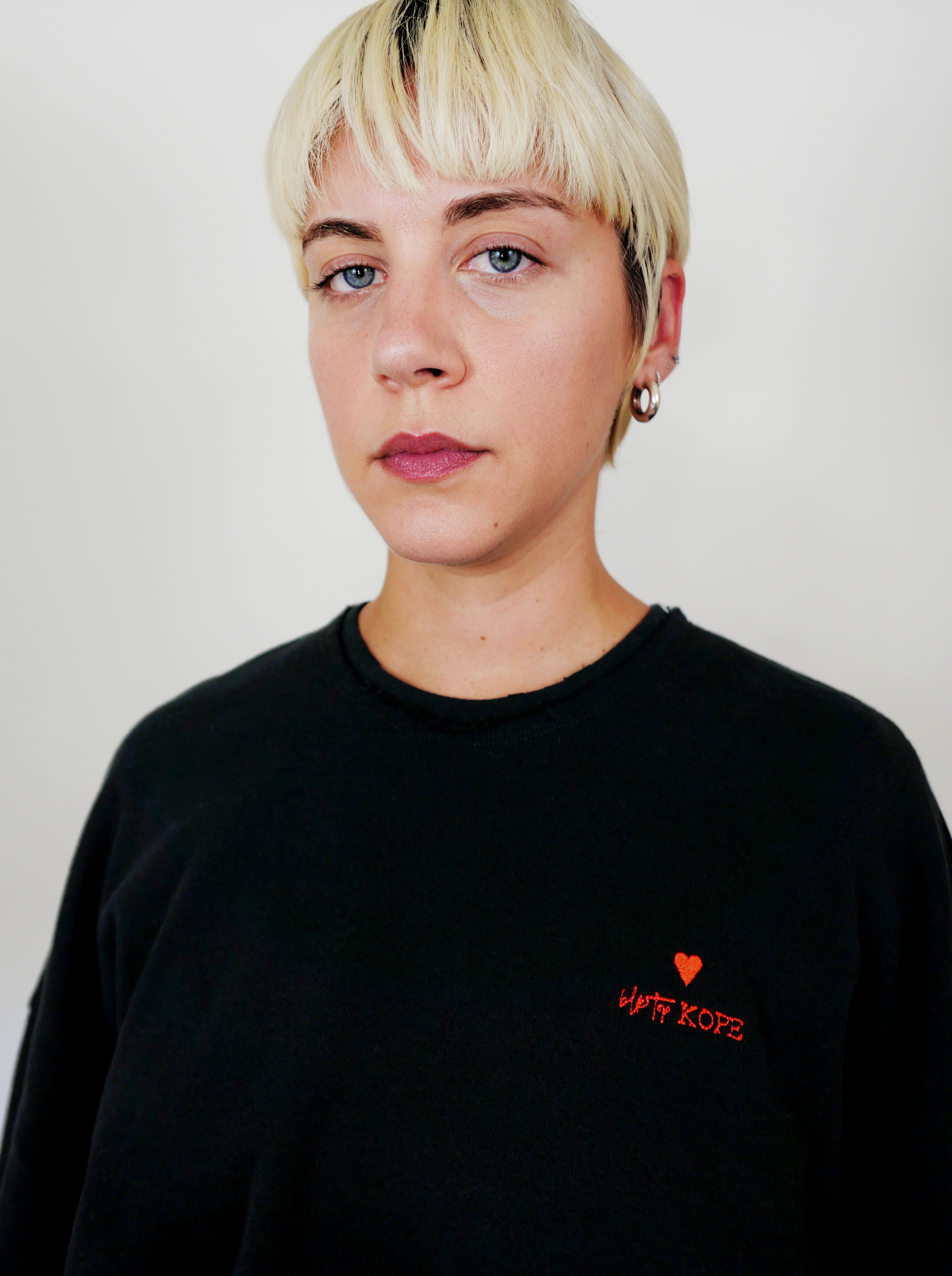 Woman wearing a black sweatshirt with a red heart and text on a plain background