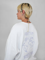 Person wearing a white sweatshirt with a world map design and text on the back, standing against a plain background.