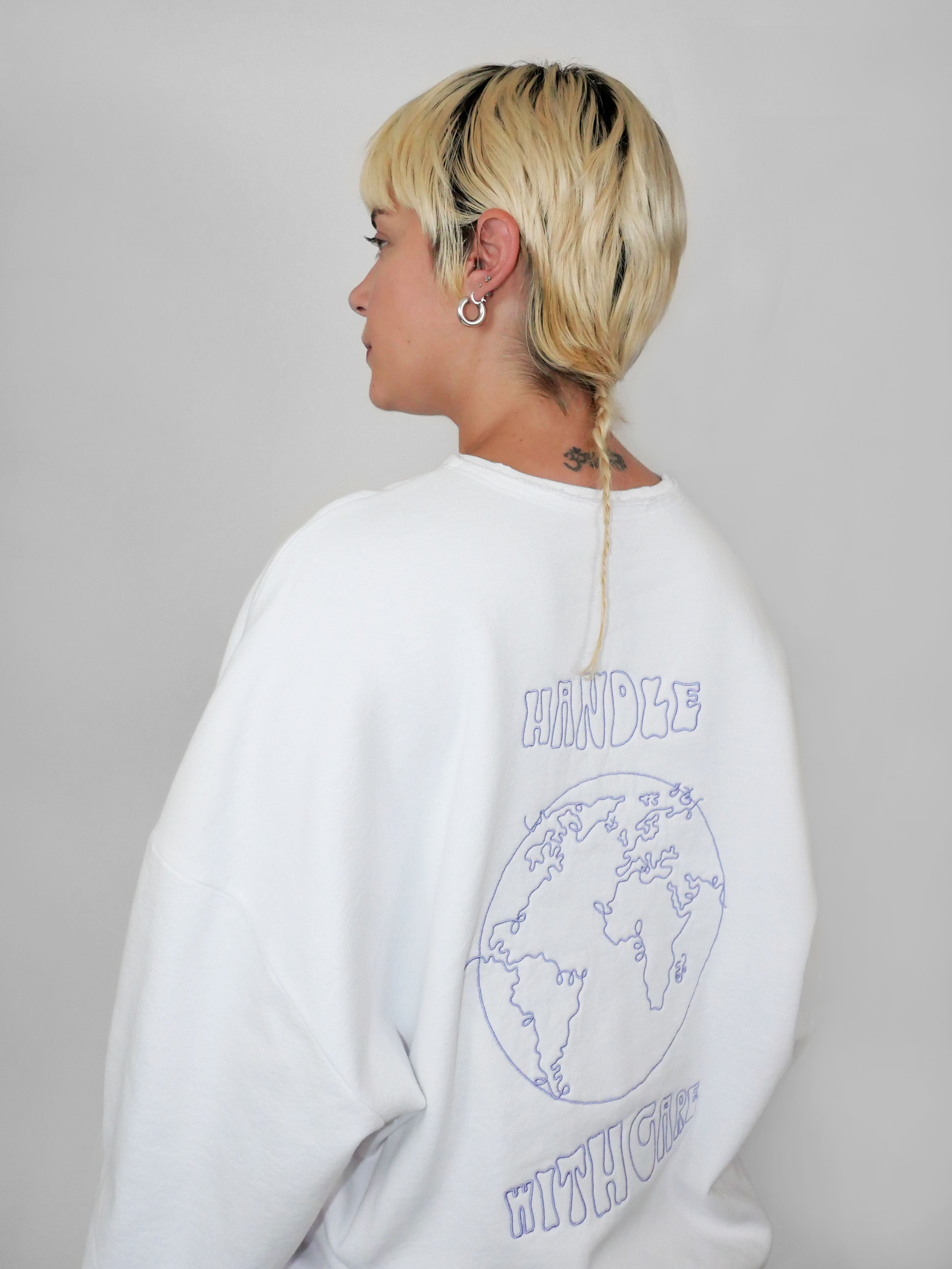 Person wearing a white sweatshirt with a world map design and text on the back, standing against a plain background.