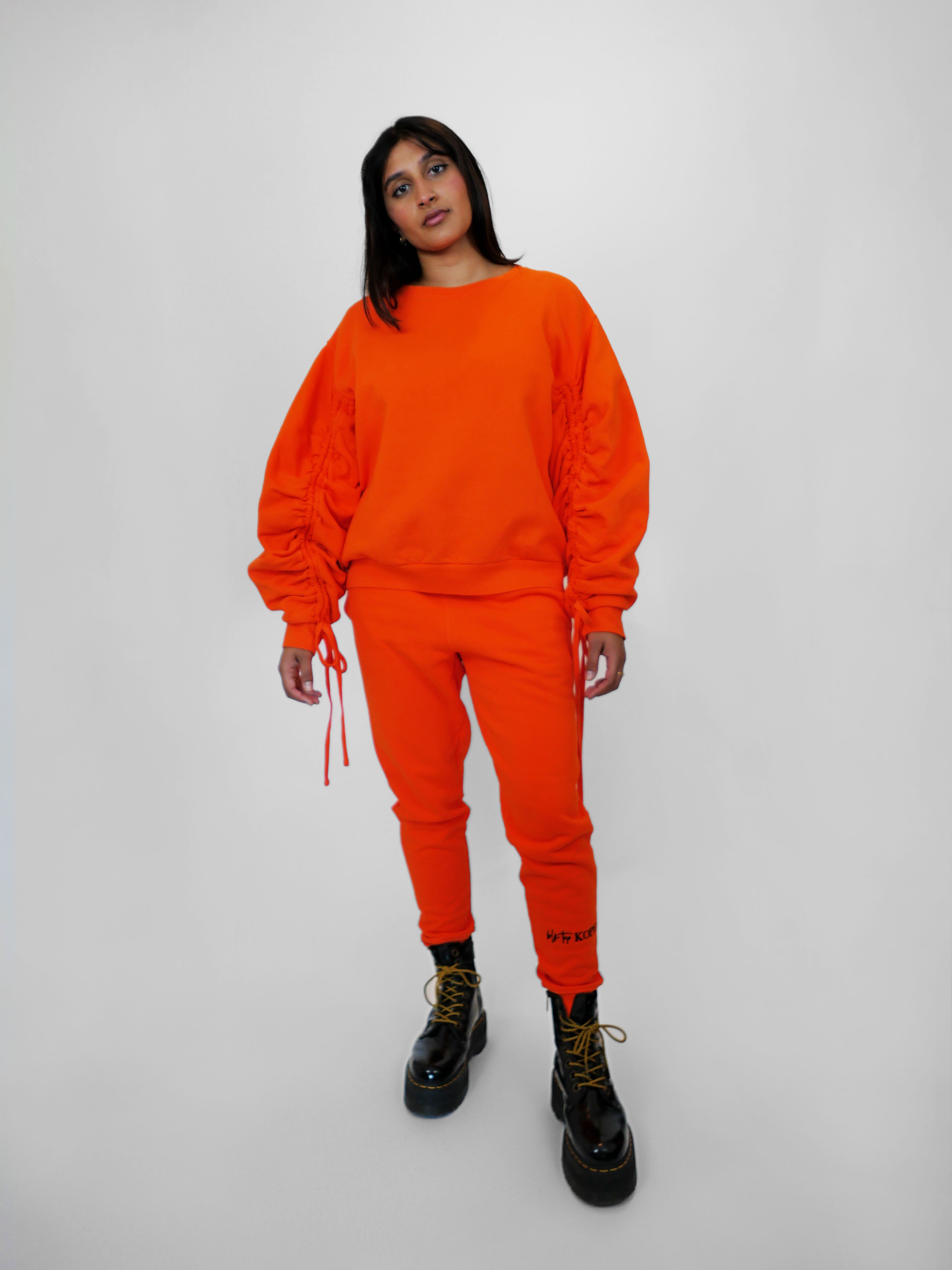 Person wearing an orange outfit with black boots on a white background