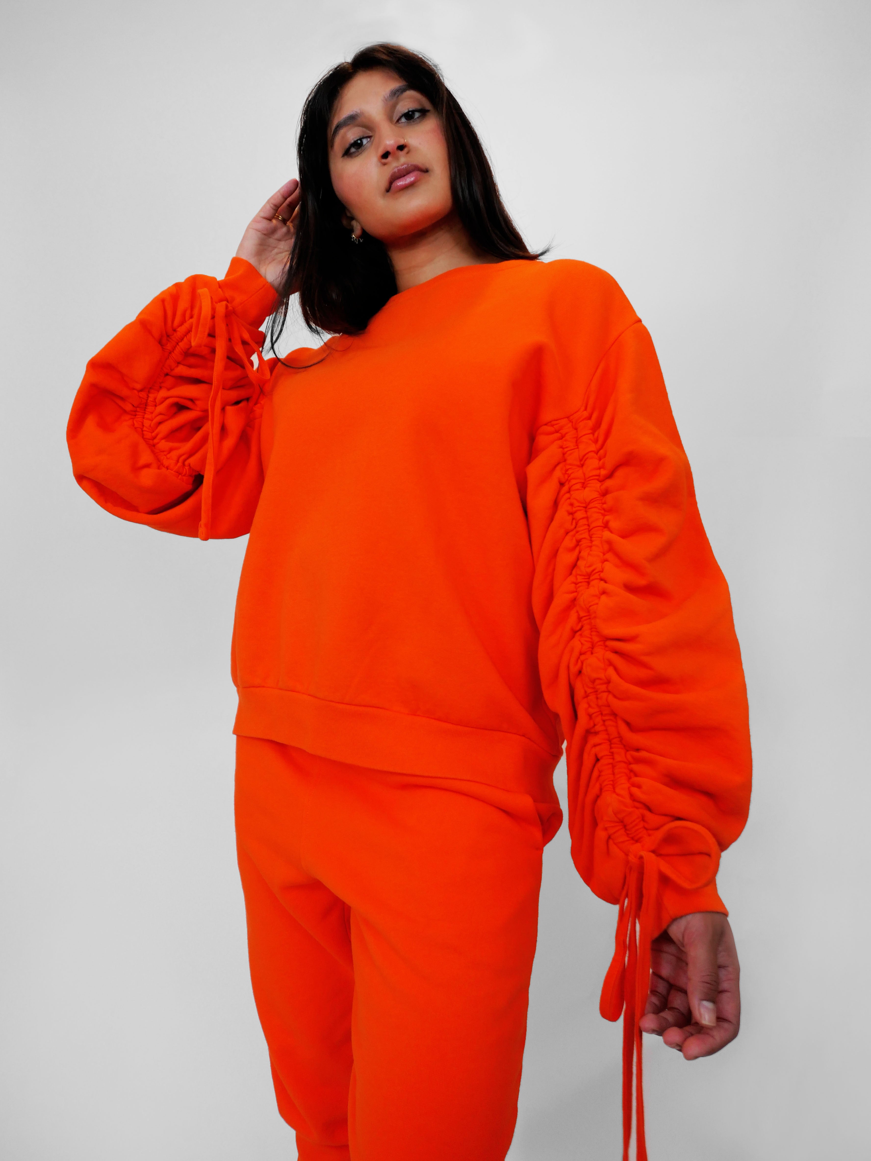 Person wearing an orange crewneck with ruched sleeves on a plain background