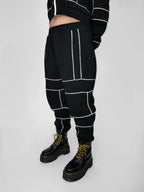 Person wearing black sweatpants with white piping and black boots on a light gray background