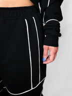 Black sweatpants with white piping worn by a person on a plain background