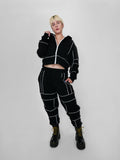 Person wearing a black tracksuit with white piping on a plain background