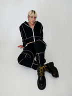 Person wearing a black tracksuit with white piping and black boots on a white background