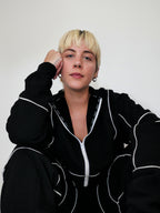 Person wearing a black full zip hoodie with white piping against a plain background