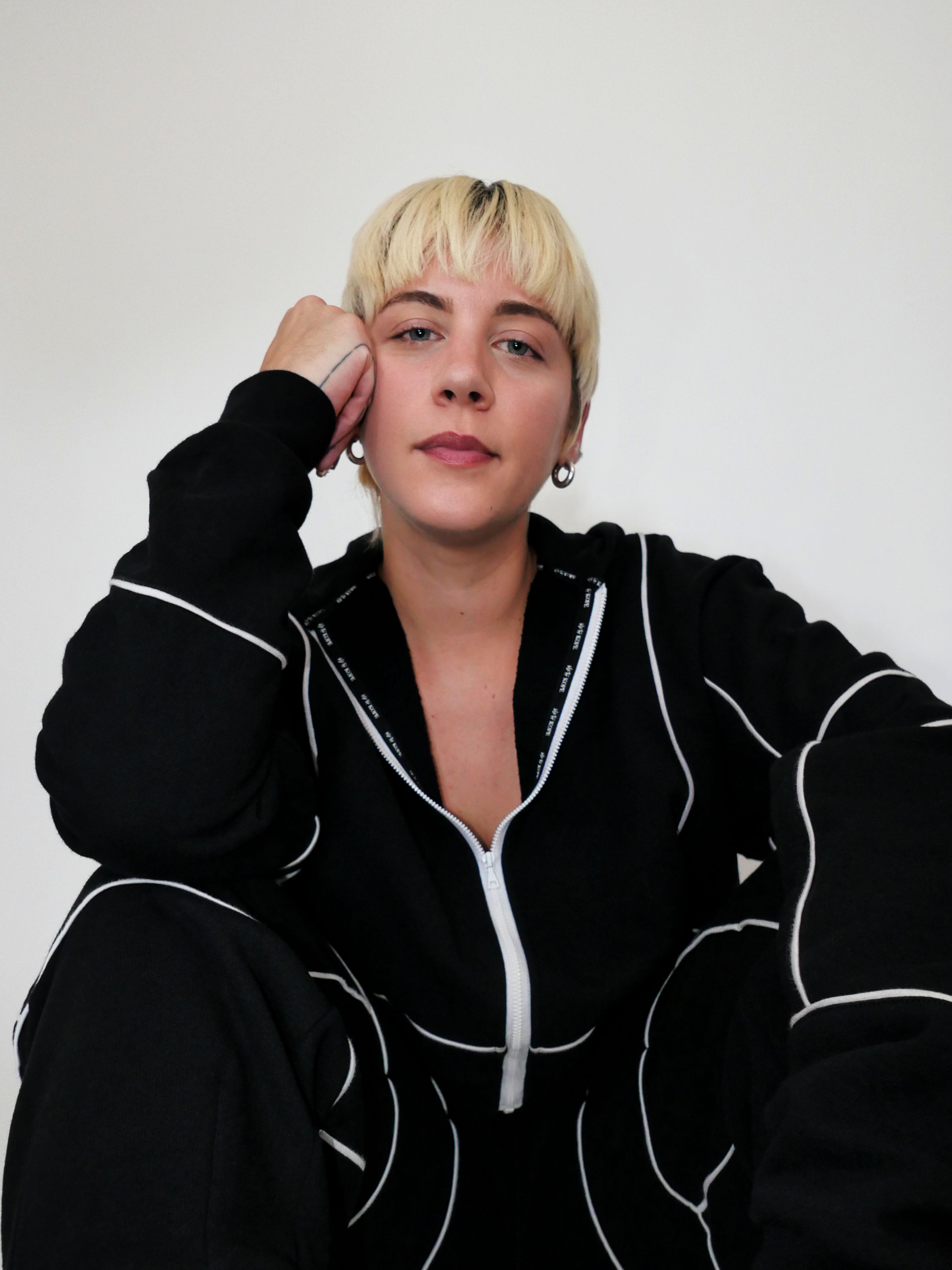 Person wearing a black full zip hoodie with white piping against a plain background