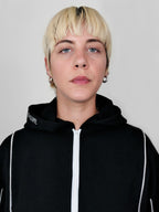 Person wearing a black full zip hoodie with a white zipper against a plain background