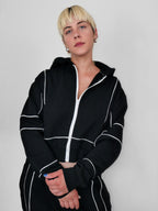 Person wearing a black full zip hoodie with white piping against a plain background