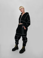 Person wearing a black tracksuit with white piping on a plain background
