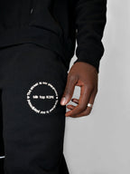 Person wearing a black outfit with a visible brand logo on a plain background