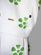 White sweatervest with green floral pattern and a brand label on a gray background