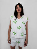 Person wearing a white sleeveless top and shorts with green floral pattern on a plain background