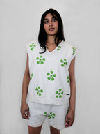 Person wearing a white sleeveless top and shorts with green floral pattern on a plain background