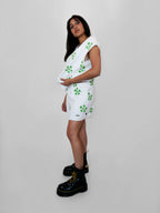 Woman wearing a white sweatervest and shorts with green floral pattern on a plain background