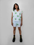 Person wearing a white sleeveless top and shorts with green floral pattern on a plain background