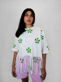 Woman wearing a white top with green floral patterns and blush pants on a plain background