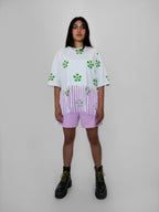 Person wearing a white oversized t-shirt with a green floral pattern and blush shorts on a plain background