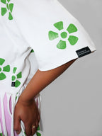 Closeup of a sleeve of a white t-shirt with green floral patterns worn by a person on a gray background
