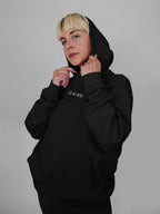Person wearing a black hoodie with a brand logo on a gray background