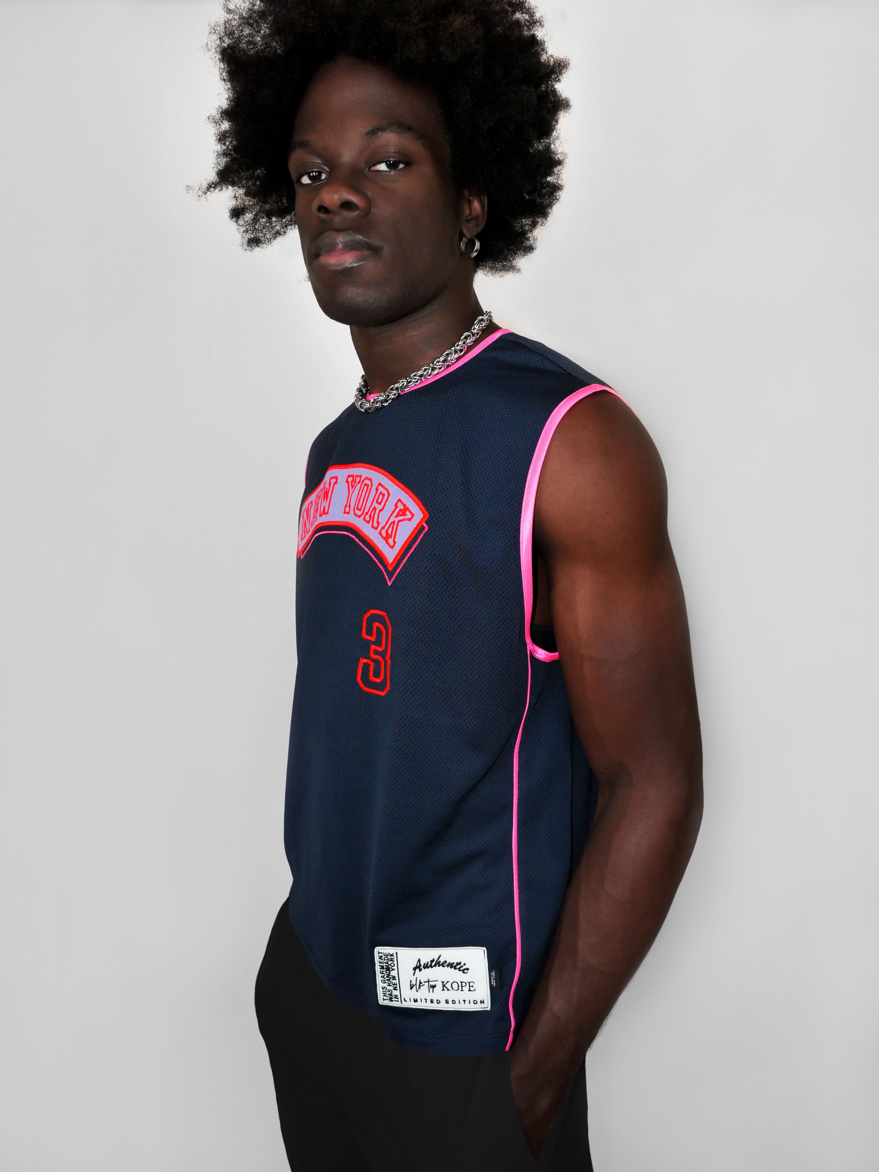 Man wearing a navy sleeveless sports jersey with red text and pink trim on a plain background