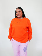 Woman wearing an orange sweatshirt and pink sweatpants with a logo against a white background