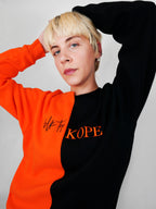 Person wearing a black and orange crewneck with 'blk top Kope' branding on a gray background
