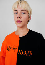 Person wearing a black and orange crewneck with 'blk top' and 'KOPE' text.