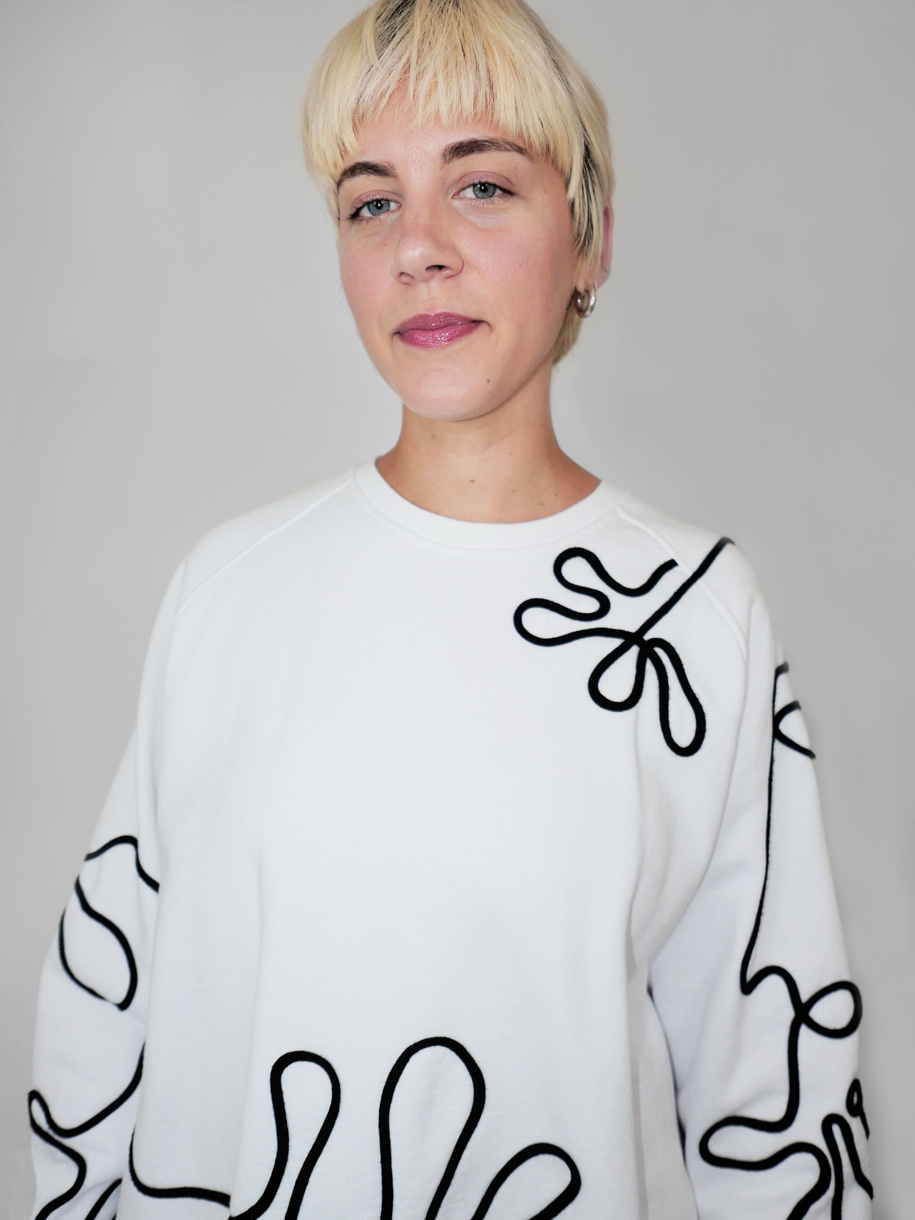 Person wearing a white sweater with black abstract one-line design against a plain background