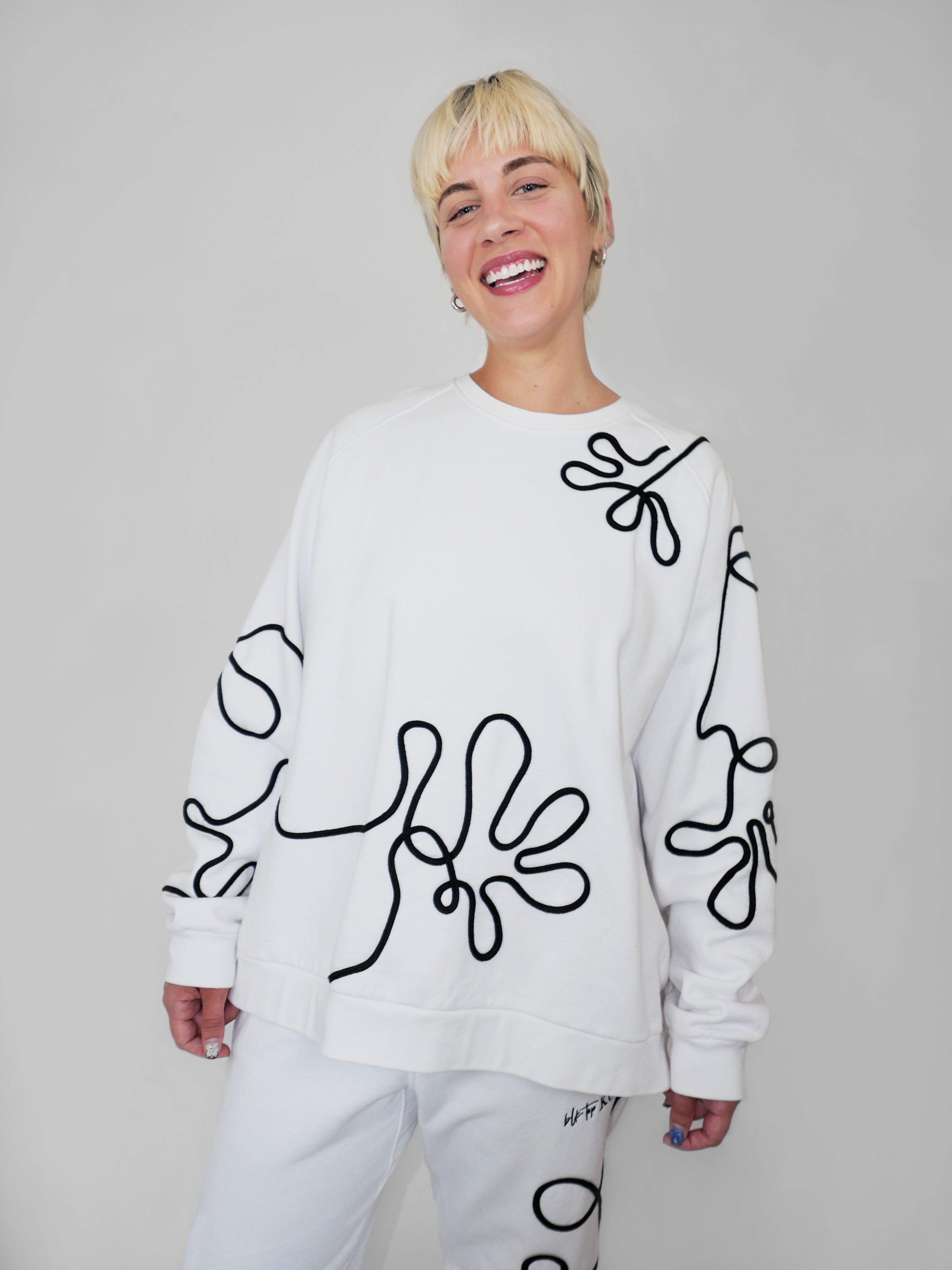 Person wearing a white sweatshirt with black abstract one-line designs on a plain background