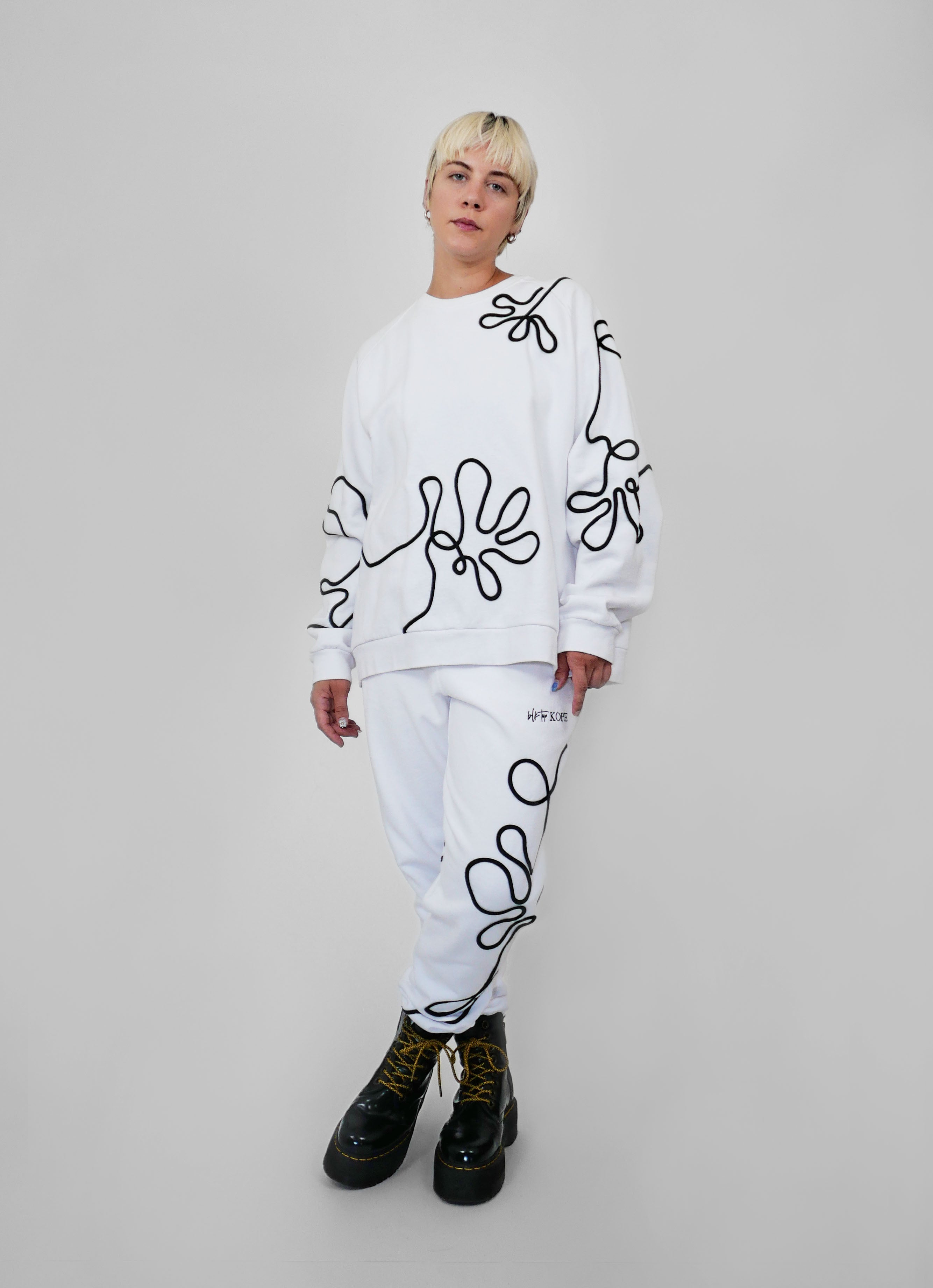 Person wearing a white outfit with black abstract one-line patterns on a plain background