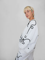 Person wearing a white sweatshirt with black abstract designs on a plain background