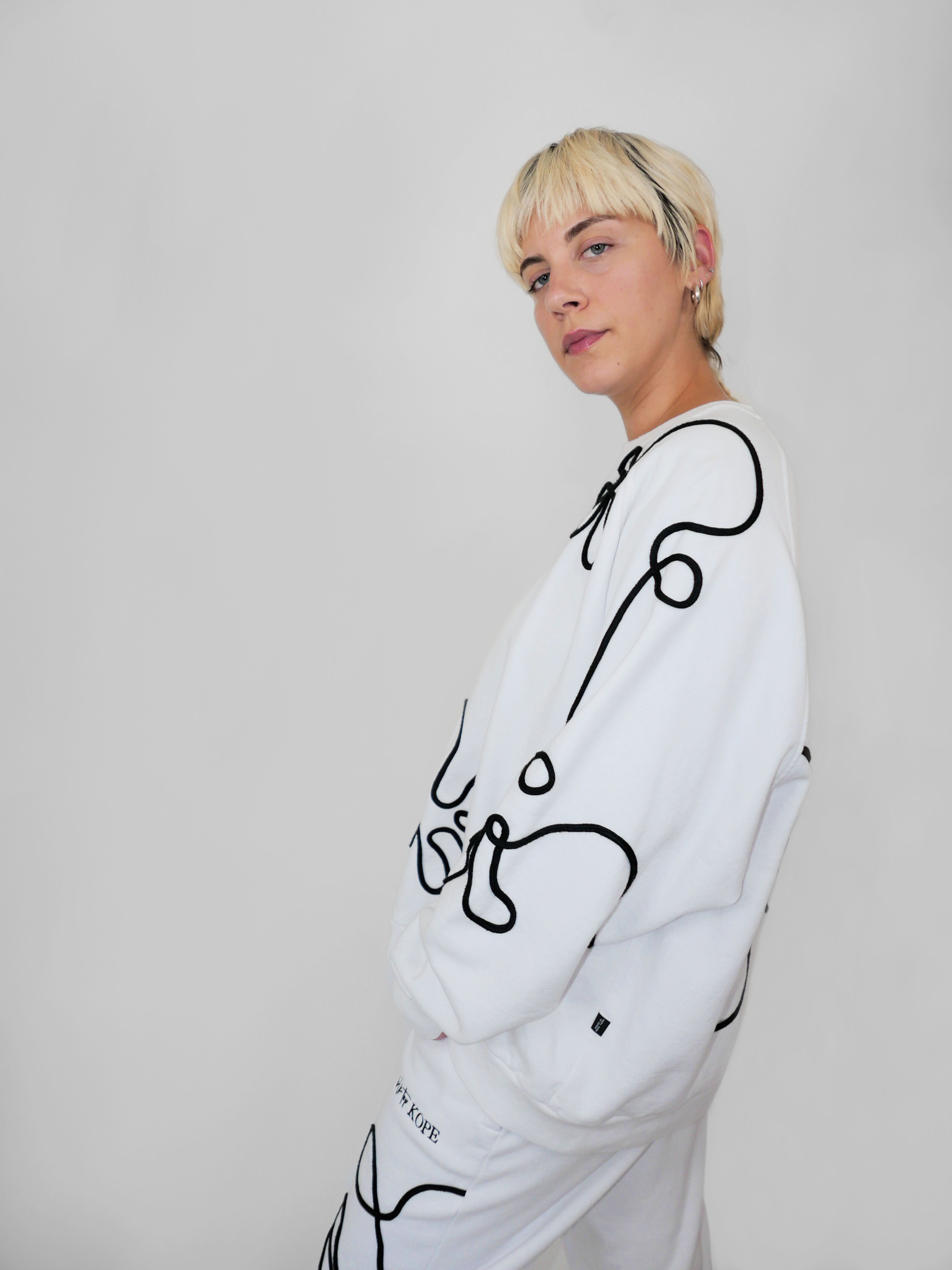 Person wearing a white sweatshirt with black abstract designs on a plain background